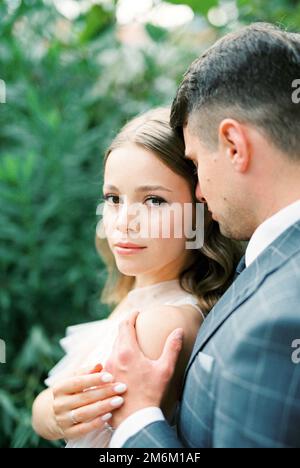 Der Bräutigam umarmt die Braut von hinten an den Schultern. Hochformat Stockfoto