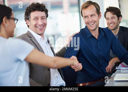 Du hast deinen Erfolg verdient. Zwei Geschäftsleute schütteln sich die Hand, während sie an einem Tisch sitzen. Stockfoto