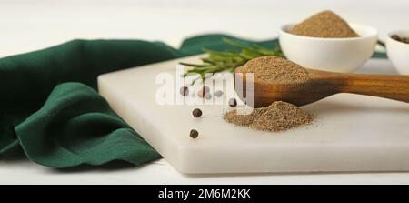 Löffel mit schwarzem Pfefferpulver auf einem hellen Tisch Stockfoto