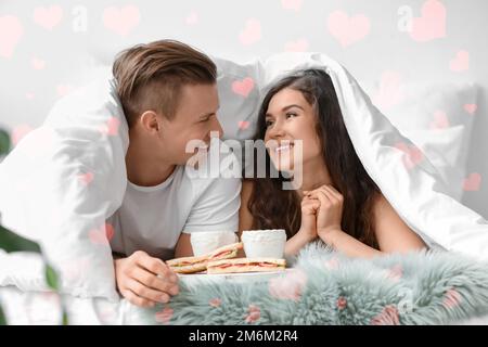 Liebendes junges Paar, das zu Hause im Bett frühstückt Stockfoto