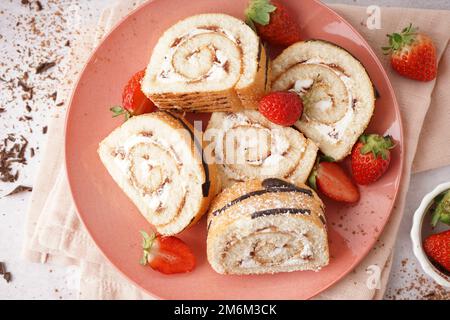 Rosafarbener Teller mit köstlichen Schwammkuchenrollen, frischen Erdbeeren, Serviette und Schokolade auf hellem Hintergrund Stockfoto