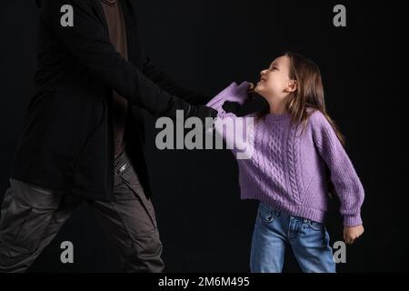 Terrorist und ängstliche kleine Geisel auf dunklem Hintergrund Stockfoto