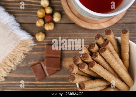 Teller mit leckeren Waffeln, Schokolade, Tasse Tee und Nüssen auf Holzhintergrund, Nahaufnahme Stockfoto