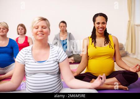 Mein Mantra ist Mutterschaft. Eine multiethnische Gruppe schwangerer Frauen, die in einem Yoga-Kurs meditieren. Stockfoto