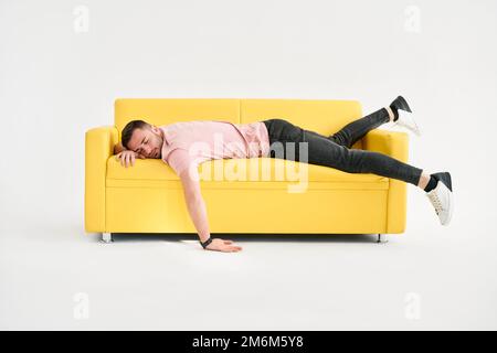 Komischer frustrierter, erschöpfter Mann, der auf dem Sofa vor weißem Hintergrund schläft Stockfoto