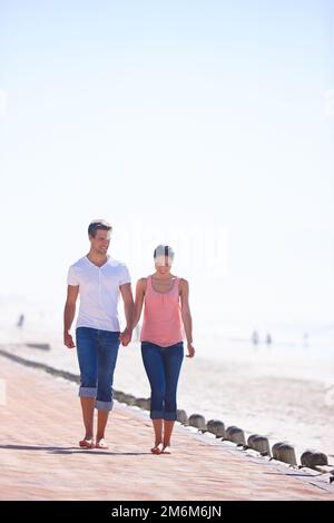 Schönheit und der Strand. Die ganze Länge eines attraktiven jungen Paares, das am Meer spaziert. Stockfoto