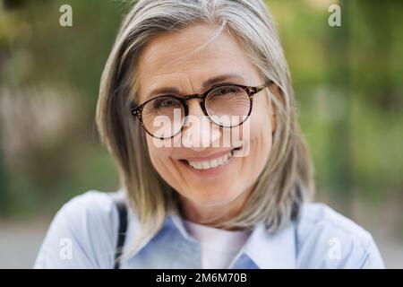 Nahaufnahme des Porträts einer charmanten, grauhaarigen, reifen Frau in Brille, die draußen steht und Urlaub in der freien Zeit auf Reisen rund um wo genießt Stockfoto