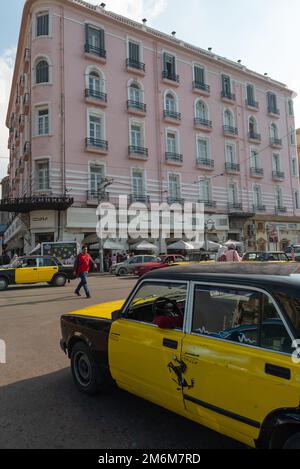 Alexandria, Ägypten. Dezember 4. 2022 Ein schwarz-gelbes Alexandria Taxi auf der Straße vor dem berühmten einst griechischen Café, dem Trianon und dem Paradise Inn, Stockfoto