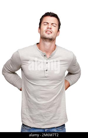 Schmerzen im unteren Rücken lähmen ihn. Ein junger Mann, der vor Schmerzen grimmt, während er seinen unteren Rücken reibt. Stockfoto