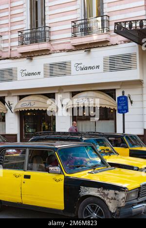 Alexandria, Ägypten. Dezember 4. 2022 Ein schwarz-gelbes Alexandria Taxi auf der Straße vor dem berühmten einst griechischen Café, dem Trianon und dem Paradise Inn, Stockfoto