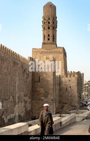 Kairo, Ägypten, November 26. 2022 ein Ägypter in traditioneller Kleidung, der vor dem Minarett der Al-Hakim-Moschee und der antiken Stadt w Stockfoto