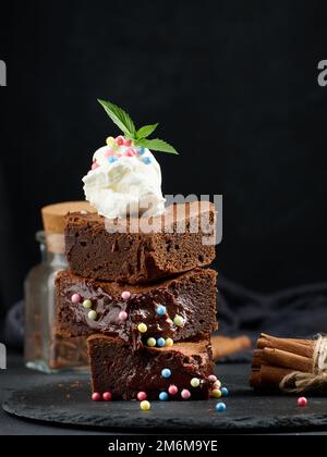 Gebackene Brownie-Schokoladenstückchen auf einem schwarzen Tisch, auf einer Kugel Eis Stockfoto