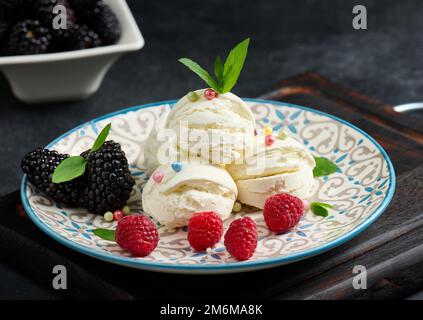 Drei Kugeln weißes Eis auf einem runden Teller mit Minzblättern auf einem schwarzen Tisch Stockfoto