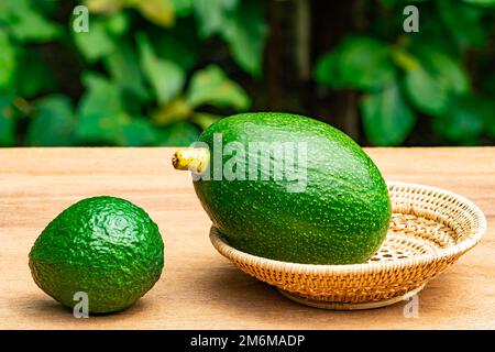 Frischer grüner Avocado in Korbbbambusbehälter auf Holztisch. Stockfoto