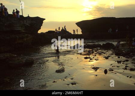 Blick auf eine felsige Strandlandschaft, wo Touristen vor Sonnenuntergang Zeit zur freien Verfügung haben, in der Nähe des Tanah Lot Tempels in Tabanan, Bali, Indonesien. Stockfoto