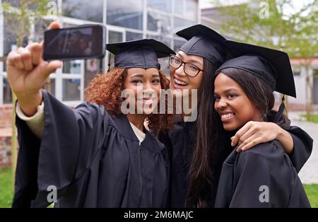 Wir haben es zur Abschlussfeier geschafft. Drei weibliche Absolventen, die sich fotografieren. Stockfoto