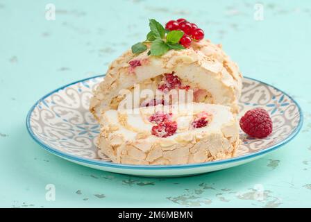 Gebackene Meringue-Rolle mit roten Beeren auf einem runden Teller, weißer Hintergrund Stockfoto