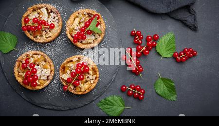 Obsttarte mit roten Johannisbeeren bestreut mit Puderzucker auf einem schwarzen Tisch, köstliches Dessert Stockfoto