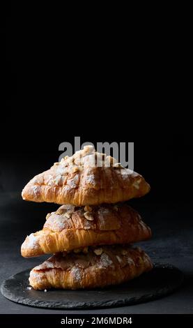 Gebackene Croissants auf einem Brett und bestreut mit Puderzucker, schwarzem Tisch. Appetitliches Gebäck zum Frühstück Stockfoto