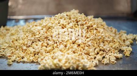 Verstreutes gesalzenes Popcorn, Texturhintergrund. Film- und Kinokonzept, Popcorn verkauft sich in einer Popcorn-Maschine, Popcorn hinter dem Glas in einer Maschine für Stockfoto