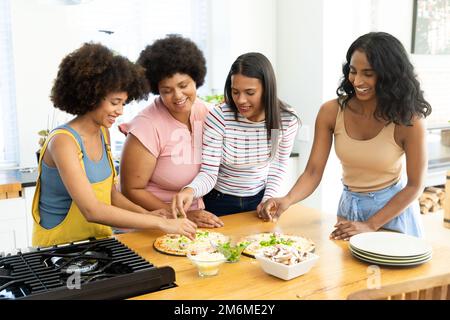 Biracial Millennial Freundinnen bereiten Pizzen auf Kücheninsel zu, während sie Freizeit verbringen Stockfoto