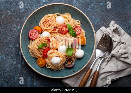 Spaghetti mit Mozzarella, bunte Kirschtomaten, frisches Basilikum auf Keramikplatte Stockfoto