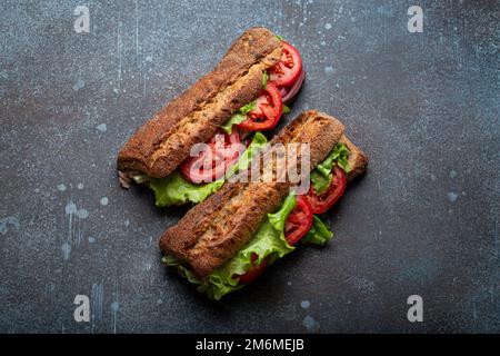 Zwei dunkle Ciabatta-Sandwiches mit grünem Salat, reifen roten Tomaten, Zwiebeln und Thunfisch Stockfoto