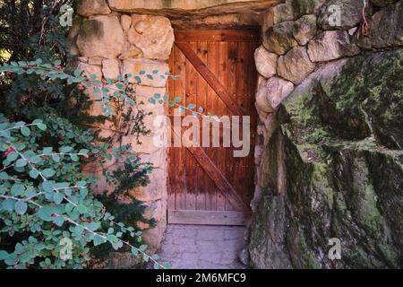 Alte braune Holzeingangstür über einer rustikalen Felswand Antike Steinmauer Stockfoto