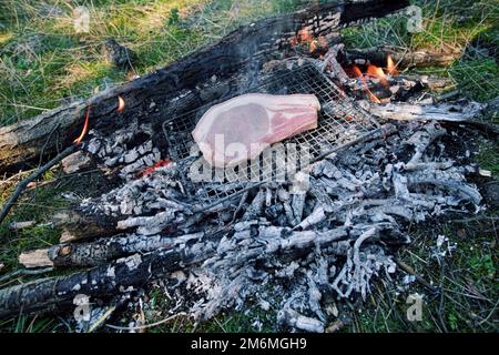Ein Schweinekotelett wird auf einem kleinen Grill auf der Glut des Lagerfeuers in Sizilien, Ätna Park, Italien geröstet Stockfoto