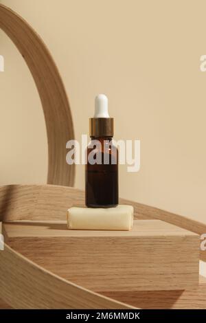 Kosmetische Braunglasflasche mit Pipette auf einem eleganten minimalistischen Holzsockel. Weibliches Schönheitskonzept. Stockfoto