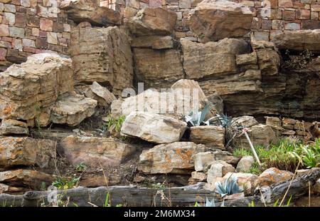 Hohe Mauer mit unterschiedlich großen quadratischen Steinblöcken mit großen Felsen davor Stockfoto