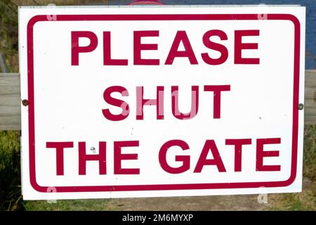 Hinweisschild mit der Aufschrift „Bitte schließen Sie das Tor“ in roter Tinte auf einer weißen Metallplatte Stockfoto