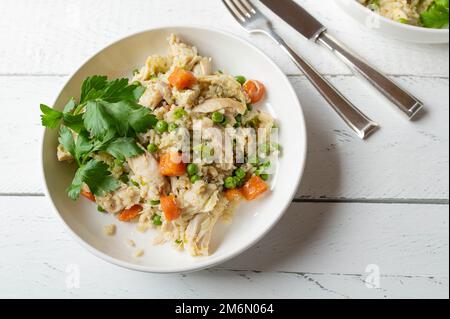 Brauner Reis mit Huhn und Gemüse auf einem Teller, isoliert auf weißem Hintergrund. Fettarme Mahlzeit für gesunde Ernährung, Diät oder Fitness Stockfoto