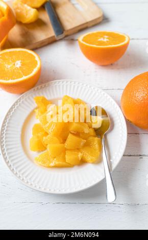 Gewürfelte oder gehackte Orangen auf einem Teller für gesunde Snacks oder Desserts auf weißem Holzhintergrund mit Schneidebrett, Schale und Messer Stockfoto