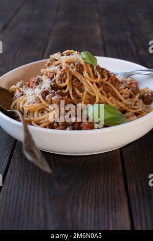 Platte mit Spaghetti Bolognese, Parmesankäse und Basilikumblättern isoliert auf dunklem Holztisch. Nahaufnahme, Vorderansicht mit Platz für Text Stockfoto