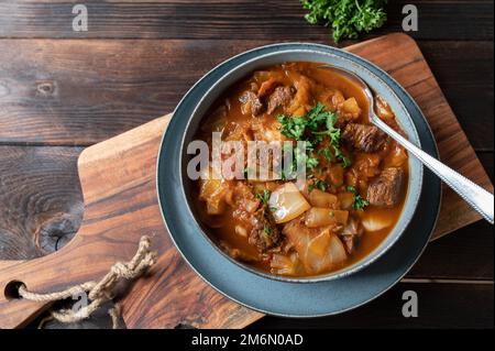 Rumänische Kohlsuppe mit Rindfleisch auf einem Holztisch. Draufsicht. Serviert in einer Schüssel mit Löffel. Stockfoto