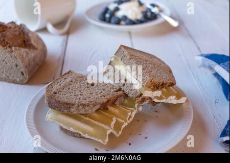 Sauerteigbrot-Sandwich mit fettarmem und eiweißarmem Quarkskäse. Serviert mit frischem Joghurt und Beeren auf einem weißen Tisch Stockfoto