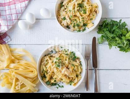 Tagliatelle-Nudeln mit Rührei und Petersilie auf Tellern, serviert auf weißem Hintergrund mit Zutaten Stockfoto