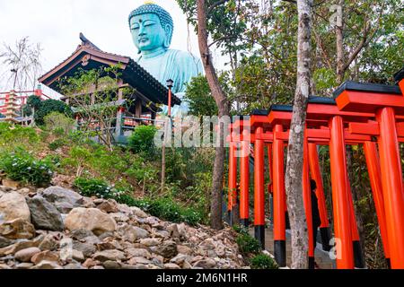 Große Buddha-Statue auf dem Berg in Doi Phra Chan in der Provinz Lampang mit dem roten Torii und einem Holzgebäude. Stockfoto