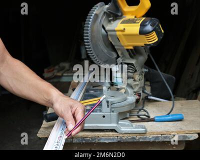 Arbeiten mit einer Gehrungssäge und Holzbohlen, Messen der richtigen Materiallänge und Markieren mit Bleistift und Lineal in einer Schreiner-Werkstatt Stockfoto