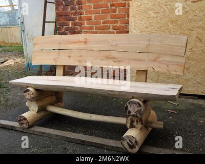 Rustikale, frisch gehobene, massive Holzbank mit wunderschöner Textur, die an der Backsteinwand im Hof steht, Gartenmöbel im Landhausstil Stockfoto