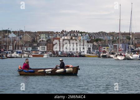 Weymouth Harbour, Dorset, Großbritannien: Ein geschäftiger kleiner Hafen mit Booten am Kai und der historischen Ruderfähre im Vordergrund Stockfoto