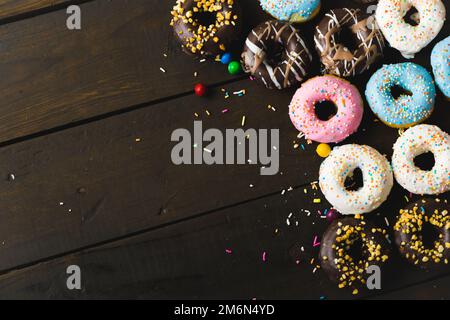 Direkt über der Ansicht von frischen verschiedenen Donuts mit Sprinklern und Bonbons auf Holztisch Stockfoto
