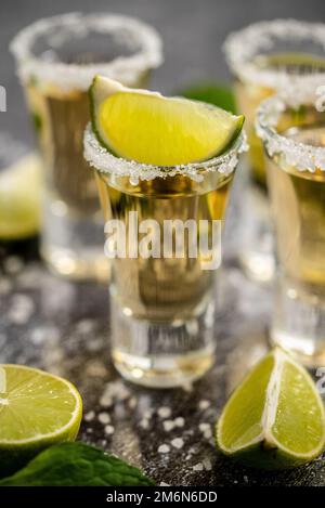 Golden Tequila Shots serviert mit Kalk und Meersalz auf dem Tisch Stockfoto