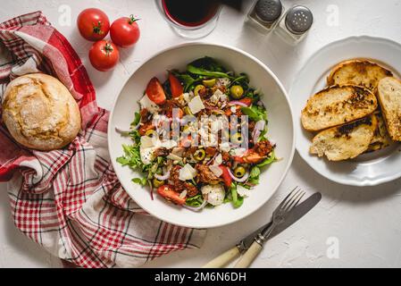 Leckerer Salat aus getrockneten Tomaten mit frischem Gemüsemix und Mozzarella-Käse, serviert mit Toast Stockfoto