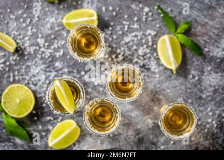 Draufsicht auf Golden Tequila Shots serviert mit Kalk und Meersalz auf dem Tisch Stockfoto