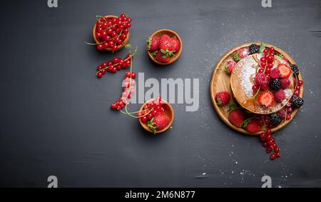 Ein Stapel Pfannkuchen mit frischem Obst, gegossen mit Sirup auf schwarzem Hintergrund Stockfoto