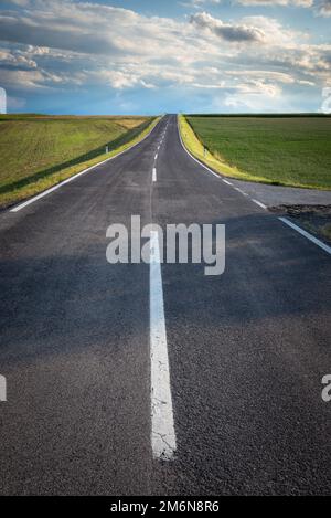 Die Betonstraße, die durch die Landschaft führt, mit natürlicher Landschaft aus Wäldern und landwirtschaftlichen Feldern. Land Stockfoto