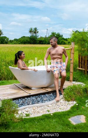 Männer und Frauen in der Badewanne draußen im Urlaub in einer Gastfamilie in Thailand mit grünem Reisfeld Stockfoto