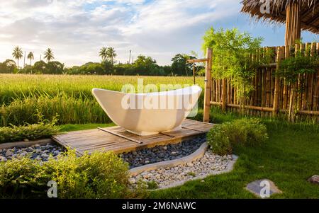 Weiße Badewanne draußen im Urlaub in einer Gastfamilie in Thailand mit grünem Reisfeld Stockfoto